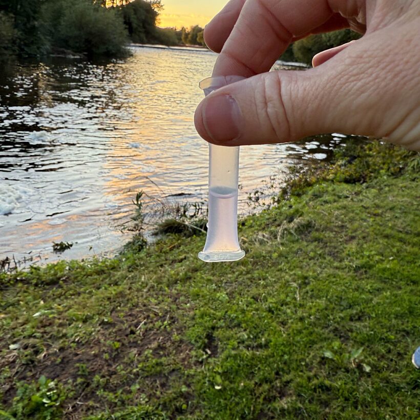 Hand holding small tube of water up in front of a river