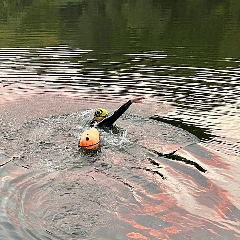 Swimmer in black wetsuit in a river towing an orange floatie