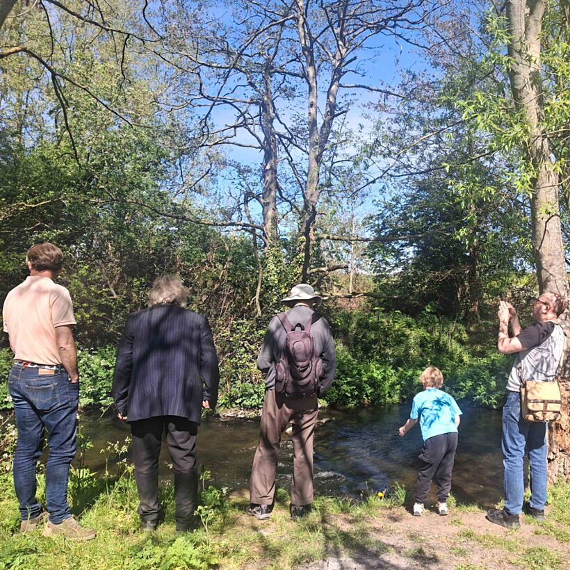 Back view of a group of people of different ages stood on a riverbank looking at the water