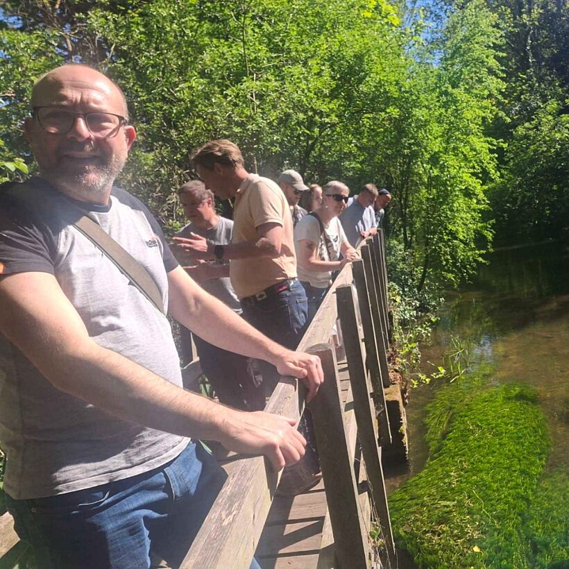 Group of people stood on a wooden bridge over a river, looking at the water