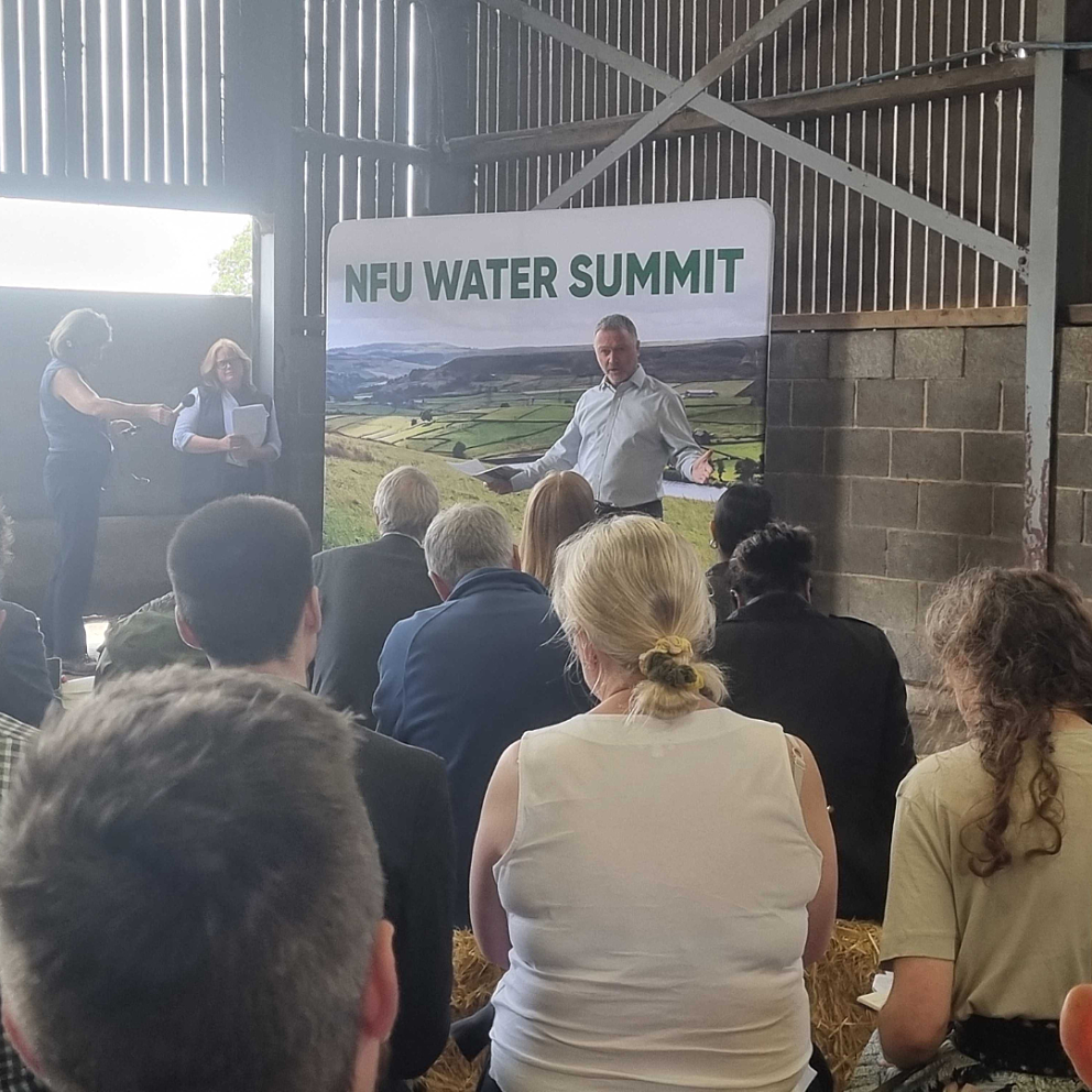 People in foreground attending a talk in a barn with a banner above the presenter reading NFU Water Summit.