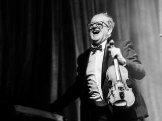 A black and white portrait photograph of Keith Pascoe holding a violin