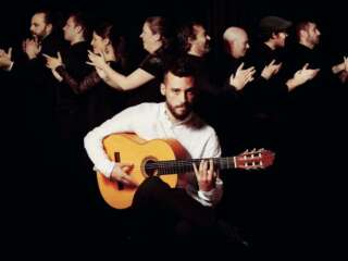 photograph of Daniel Martinez playing the guitar in front of eight flamenco dancers clapping