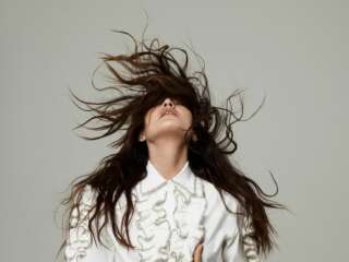Joan As Police Woman, in a white shirt against a beige backdrop
