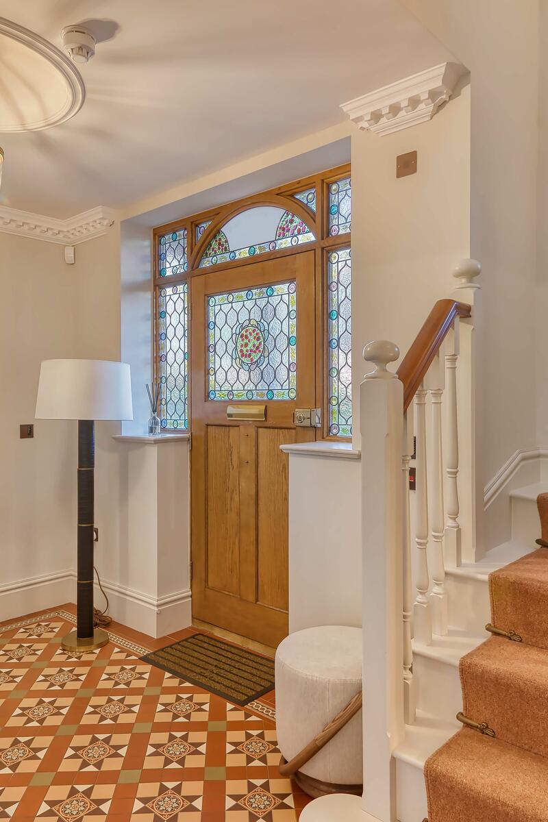 Bright period entrance hall with stained glass front door, patterned tiled floor and staircase with traditional banister