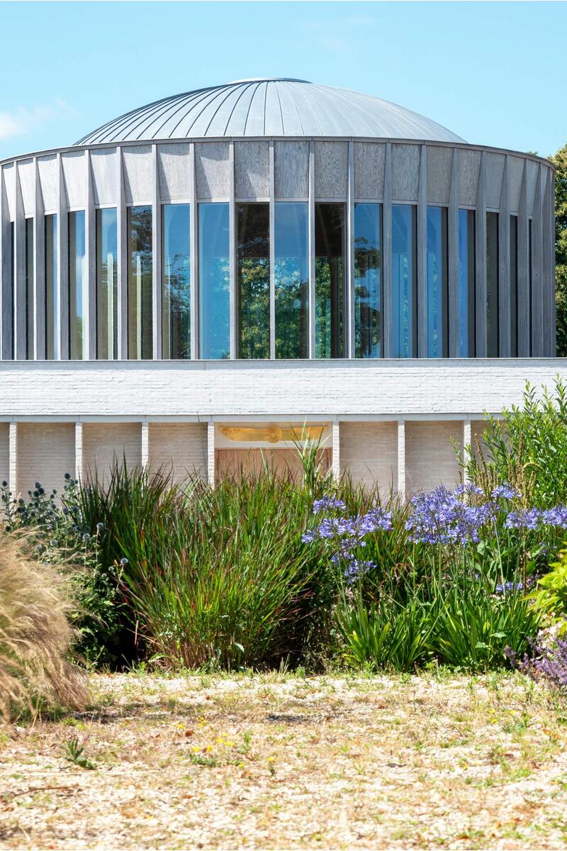 Contemporary circular pavilion with vertical glazing and domed roof set within landscaped gardens and wild planting, modern architectural shoot location UK