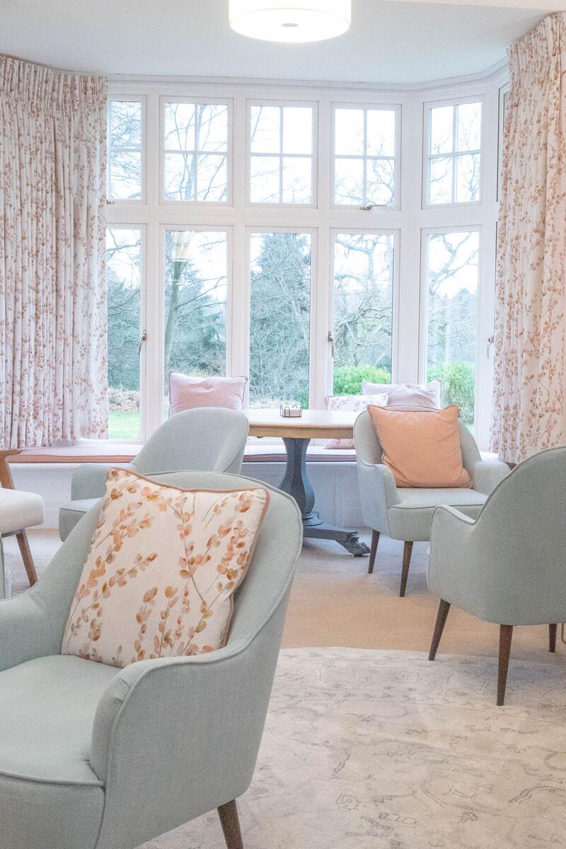 Soft pastel lounge with blush pink walls, mint green armchairs and large bay windows overlooking gardens.