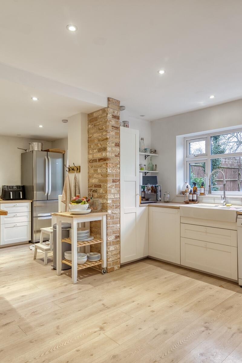 Spacious open plan family kitchen with pale shaker cabinetry, timber worktops, central island, exposed brick column and light wood flooring.