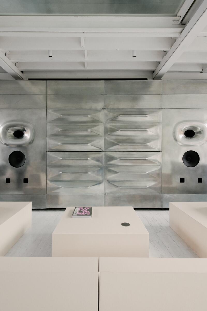 Modern industrial salon reception with sculptural stainless steel wall panels, geometric seating and white painted beams
