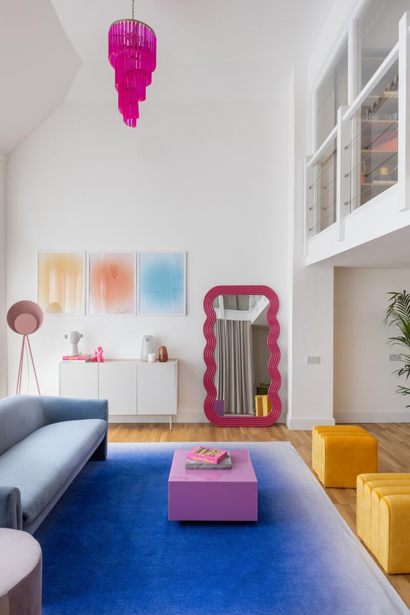 Double-height living space with blue sofa, pink chandelier, large windows and colourful contemporary styling