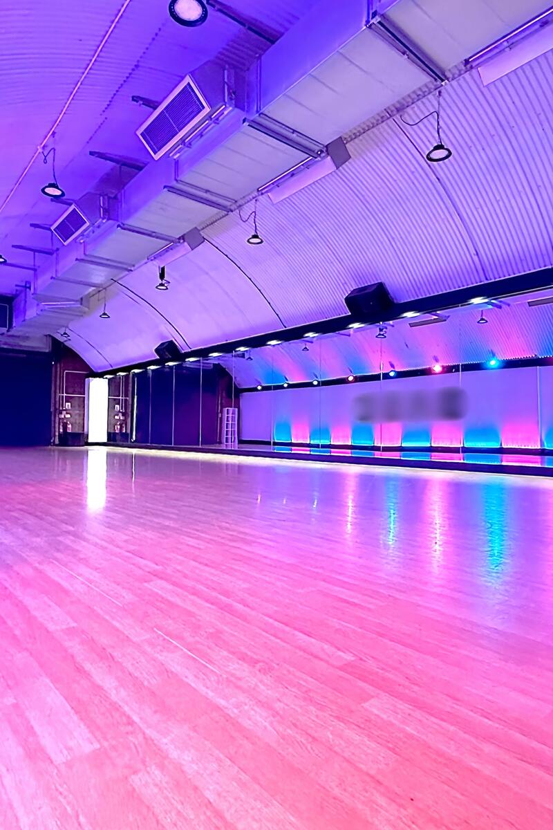 Large professional dance studio with sprung wooden flooring, vaulted ceiling and atmospheric coloured lighting.