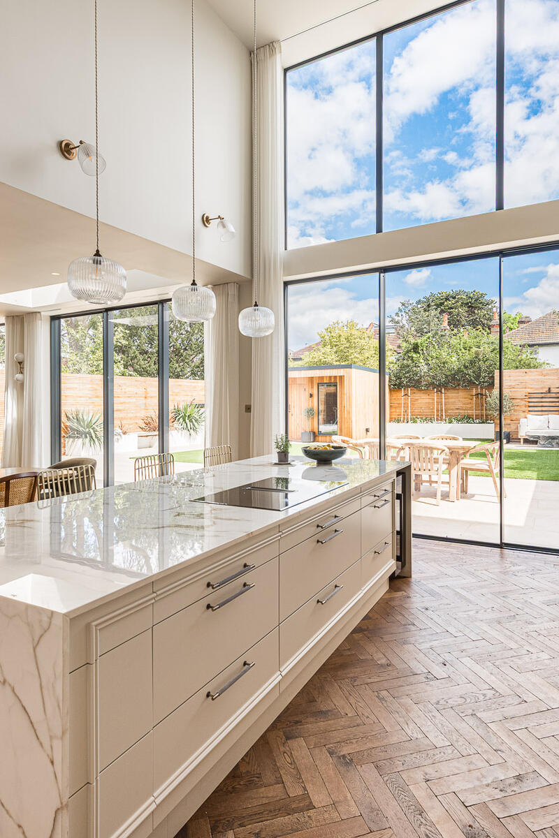 Double-height marble kitchen with large island, floor-to-ceiling glazing and open-plan living space in a contemporary Teddington family home.