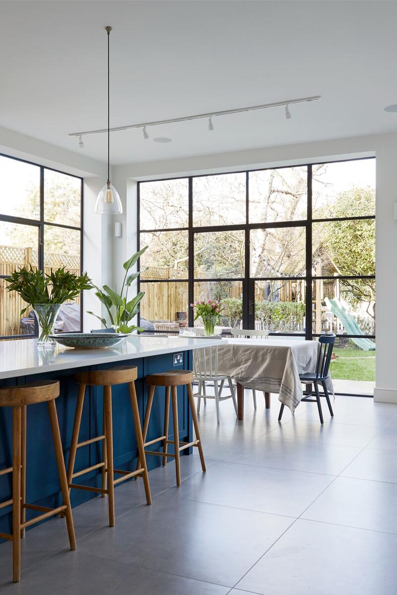 Open plan kitchen with blue island, steel-framed doors and garden views in a Victorian family home.