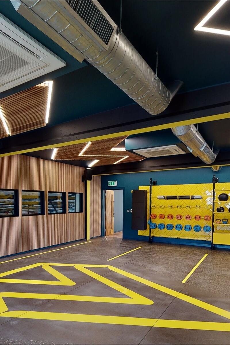Modern fitness studio with timber wall panelling, geometric lighting and functional training equipment.