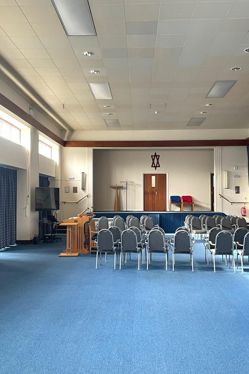 Large synagogue hall with high ceilings, stage, blue carpeting and flexible seating for filming and events.