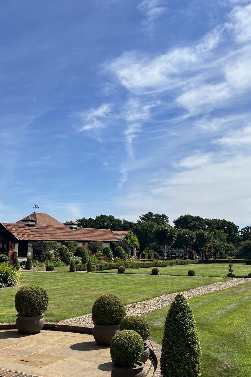Large country home filming location with extensive landscaped lawns, mature planting, topiary and gravel paths.