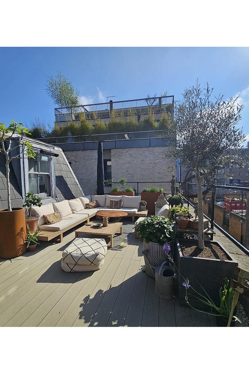 Loft apartment rooftop terrace with outdoor sofas, potted trees and urban views.