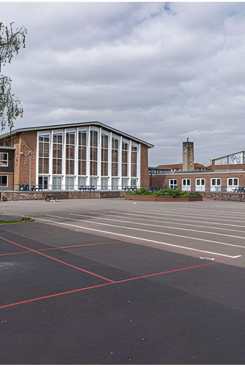 Wide view of a London secondary school exterior with red-brick buildings, large windows and an expansive marked playground.