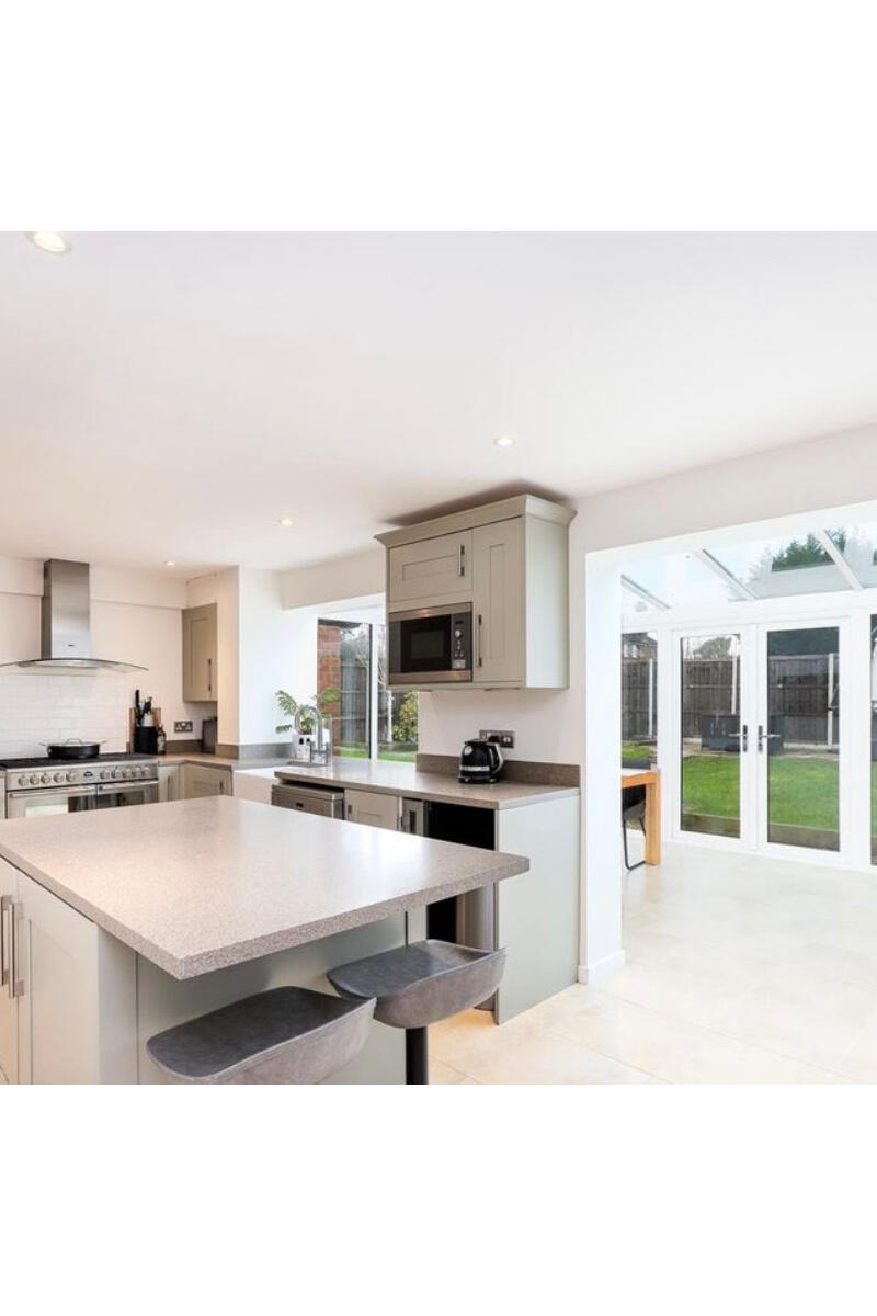 Modern open-plan kitchen with island, neutral cabinetry, range cooker, and adjoining conservatory dining area with garden access.