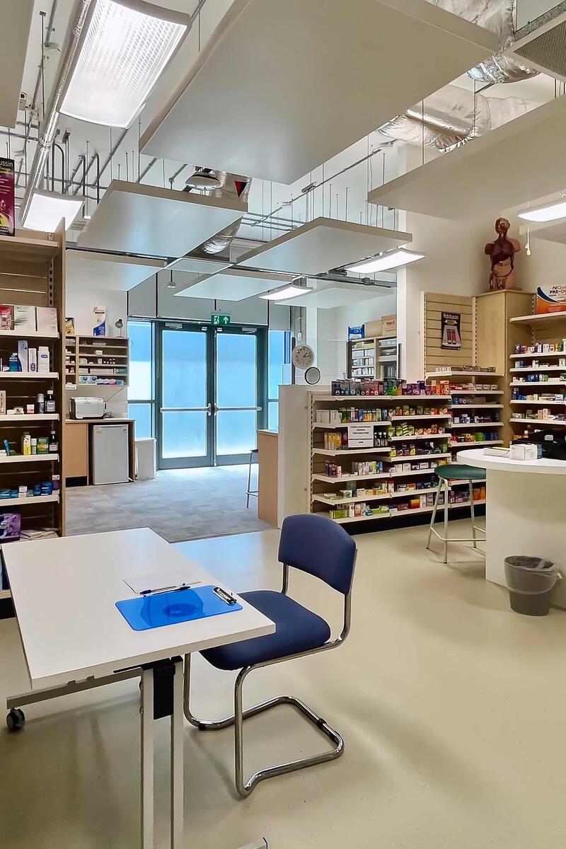 Mock pharmacy training room with fully stocked shelves, consultation desk, and customer counter, designed for realistic medical training or film shoots.