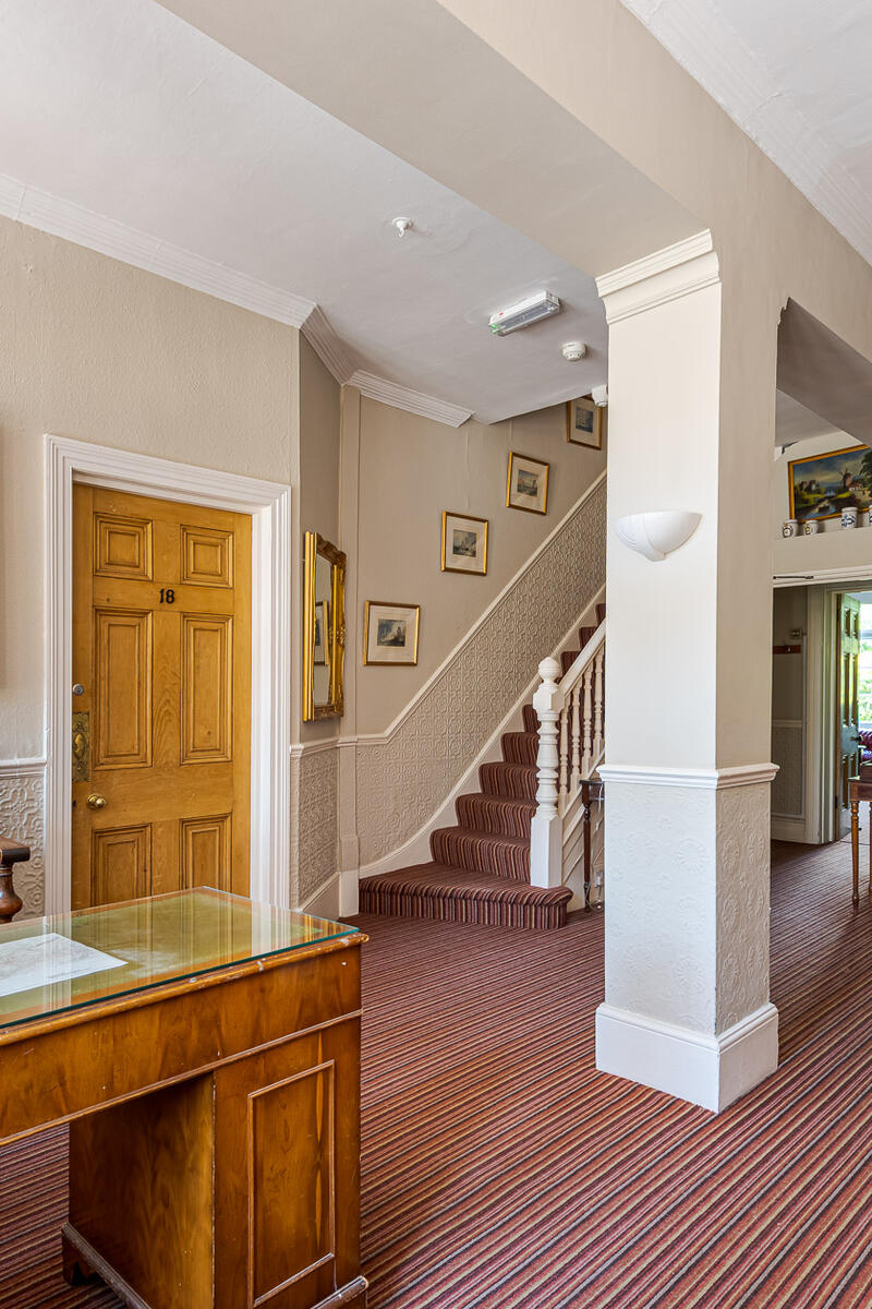 Victorian hotel hallway with reception desk, striped carpet, staircase and period details, available for film, TV and photography shoots in West London.