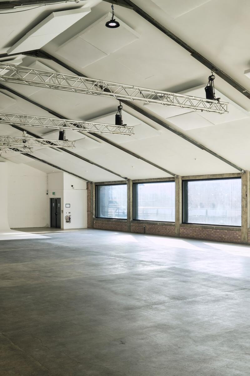 Large industrial warehouse studio in London Fields with vaulted ceilings, exposed brickwork, concrete flooring, and full-length windows.