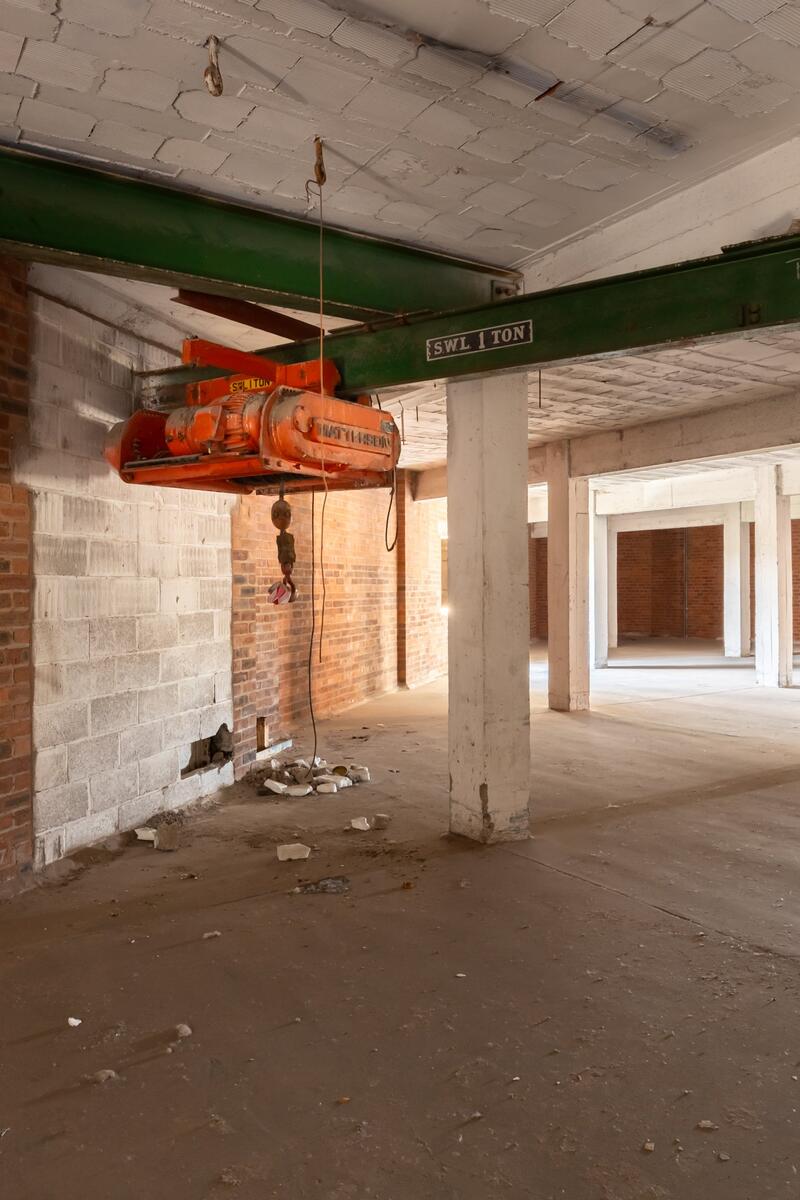 Industrial warehouse interior with exposed brick walls, concrete pillars, and overhead crane feature in Manchester.