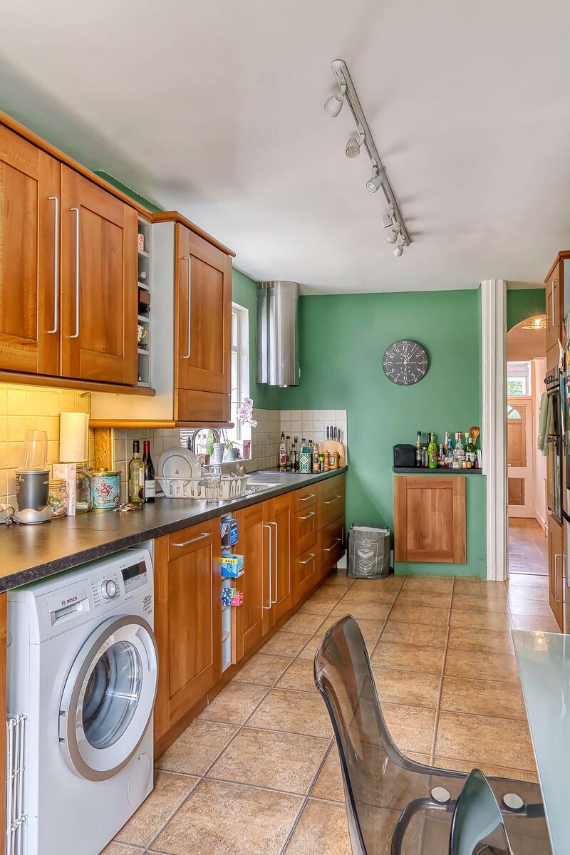 Traditional kitchen with wooden cabinets, tiled floor, green feature wall, and modern appliances including washing machine.
