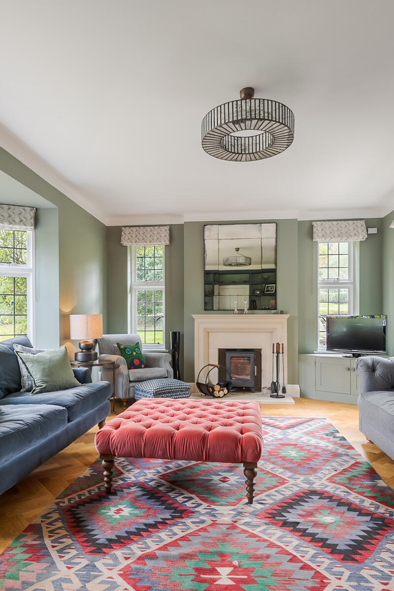 Spacious living room with green walls, bay windows, grey sofas, patterned rug, and fireplace.