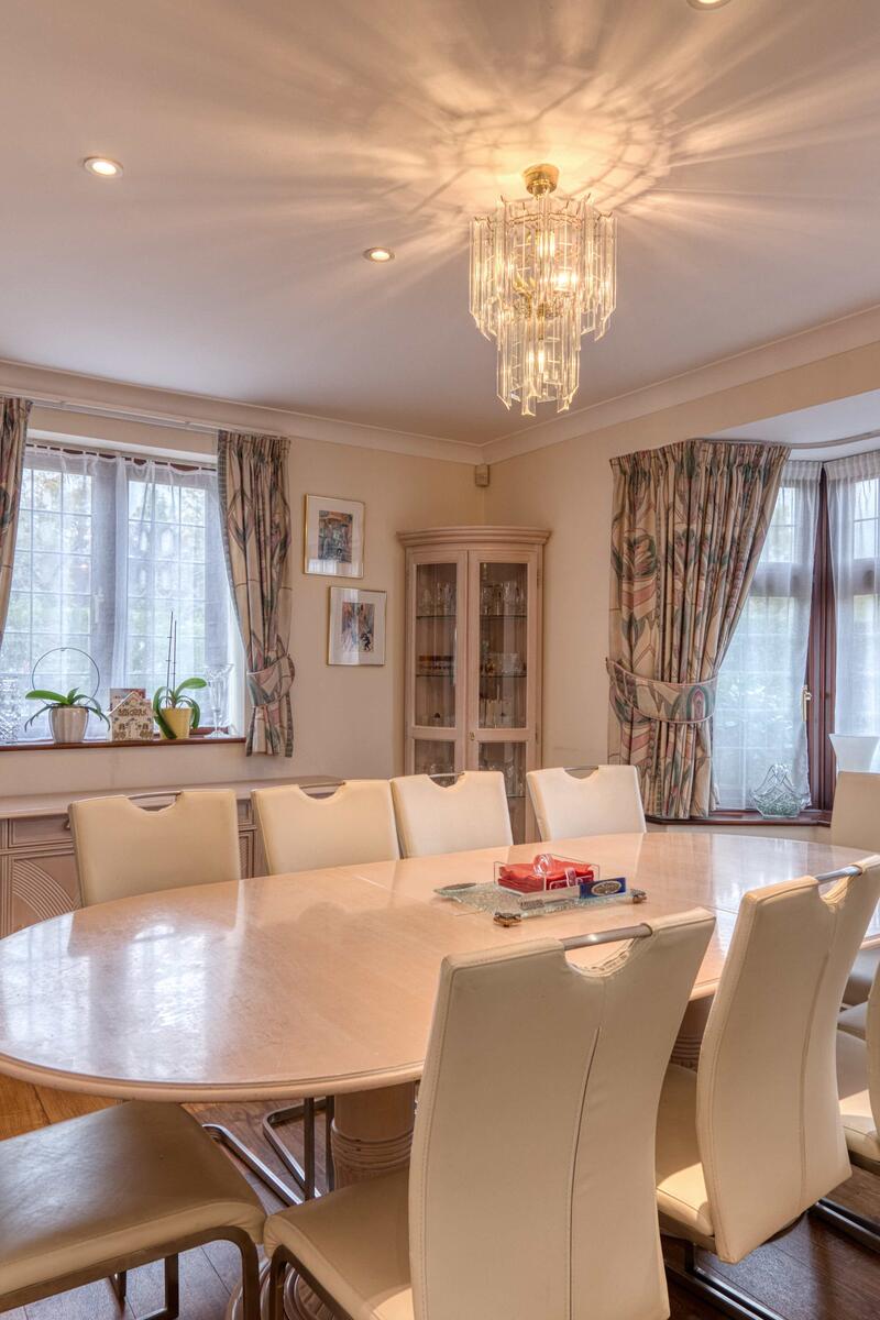 Dining room with large oval table, cream leather chairs, chandelier lighting, bay window with patterned curtains, and traditional decor.