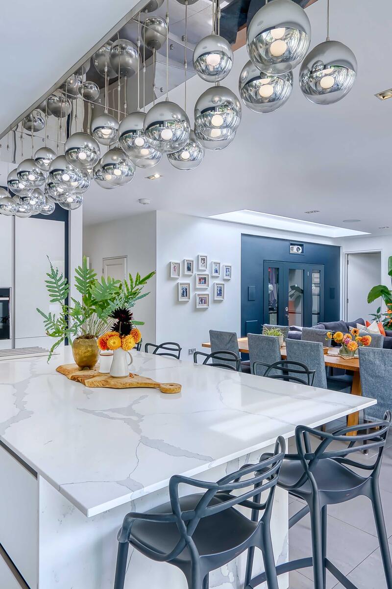 Modern open-plan kitchen and living space with white gloss cabinets, marble island, designer pendant lights, dining area and lounge seating.