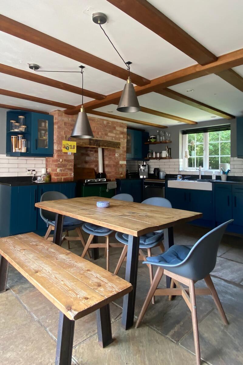 Country-style kitchen with exposed beams, blue cabinetry, brick feature wall and farmhouse dining table – film and photoshoot location.
