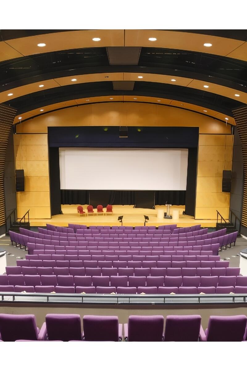 Modern university theatre in Hertfordshire with 440 raked purple seats, large stage, and curved acoustic wood panelling.
