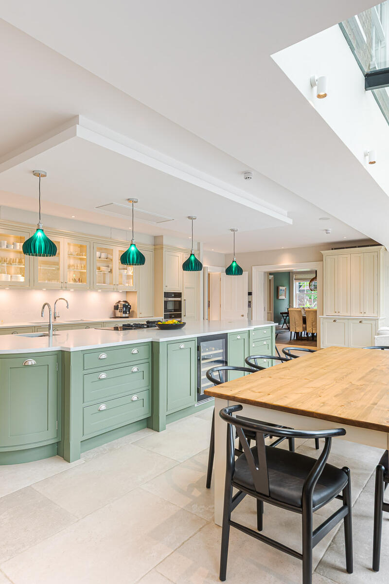 Luxury open-plan kitchen with mint-green island, pendant lights and glass roof flooding the space with natural light.
