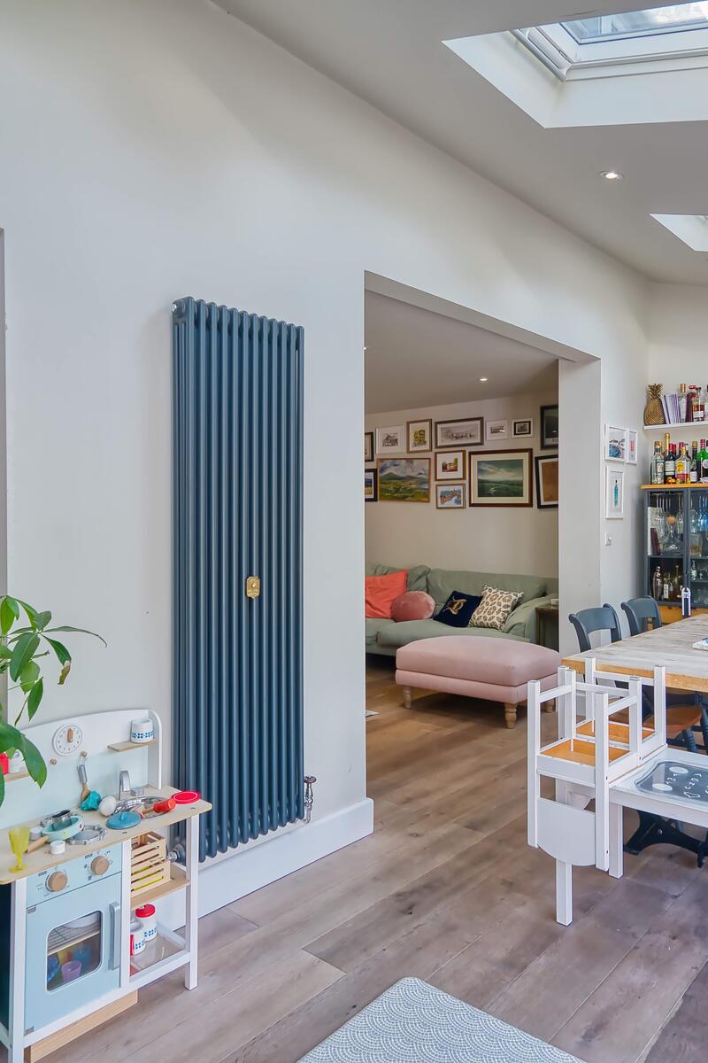 Bright open-plan kitchen, dining and family room with skylights, blue cabinetry, wooden flooring and eclectic wall art, creating a relaxed, homely atmosphere.