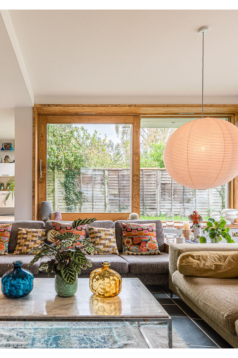 Mid-Century Modern open-plan living room with large windows, colourful cushions and paper lantern pendant light.