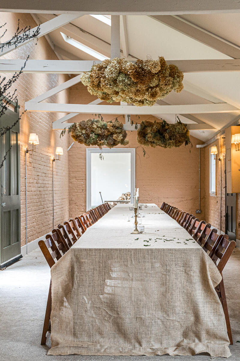 Atmospheric dining space with long linen-draped table, peach brick walls, skylights, and dried floral ceiling displays in a converted Victorian potting room.