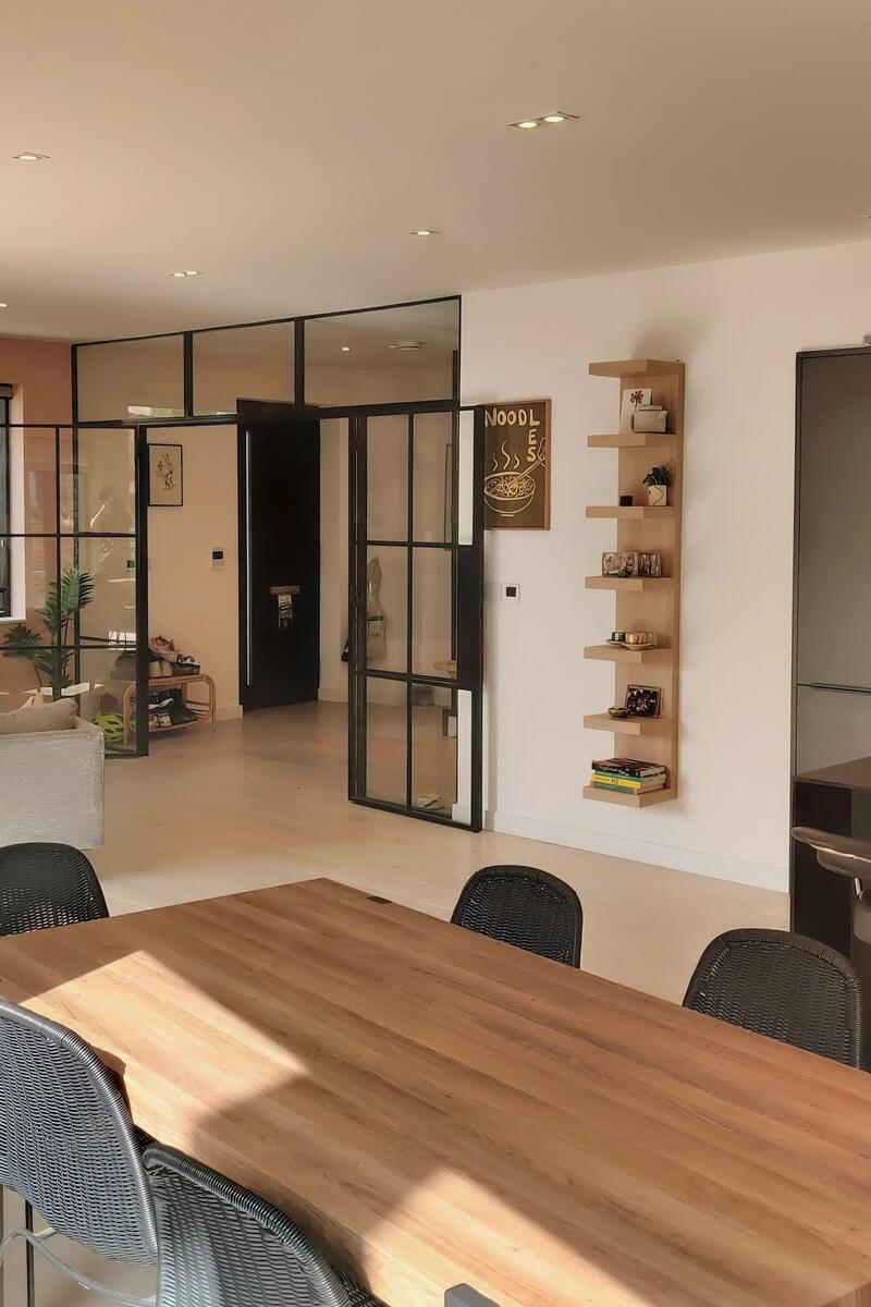Bright open plan kitchen, dining and living area with pale wood flooring, black framed internal glass doors and modern neutral decor in a contemporary Hackney flat.