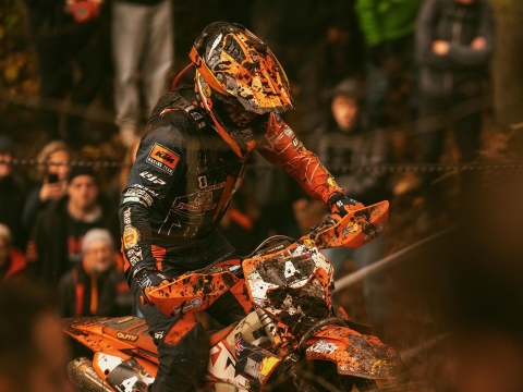 Enduro bike rider Burts Crayston riding a KTM bike covered in mud through a dark wooded area of an offroad course