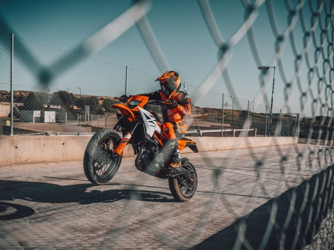 A KTM Motocycle being ridden on a race track with the rider lifting the front wheel as he accelerates.