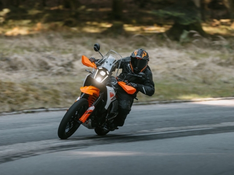 Motorcyclist riding a KTM Adventure 390 X around a bend with blur suggesting speed.