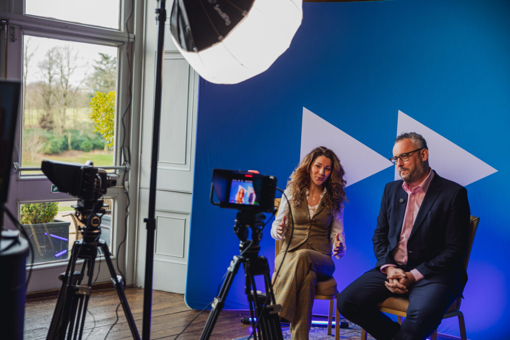 Two people in front of blue backdrop, with camera equipment around them