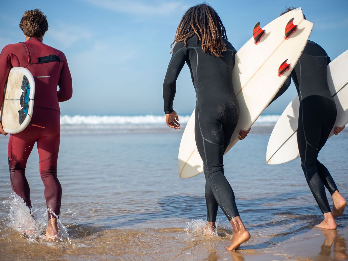 Stag group of three lads heading into the surf with their boards in Portugal