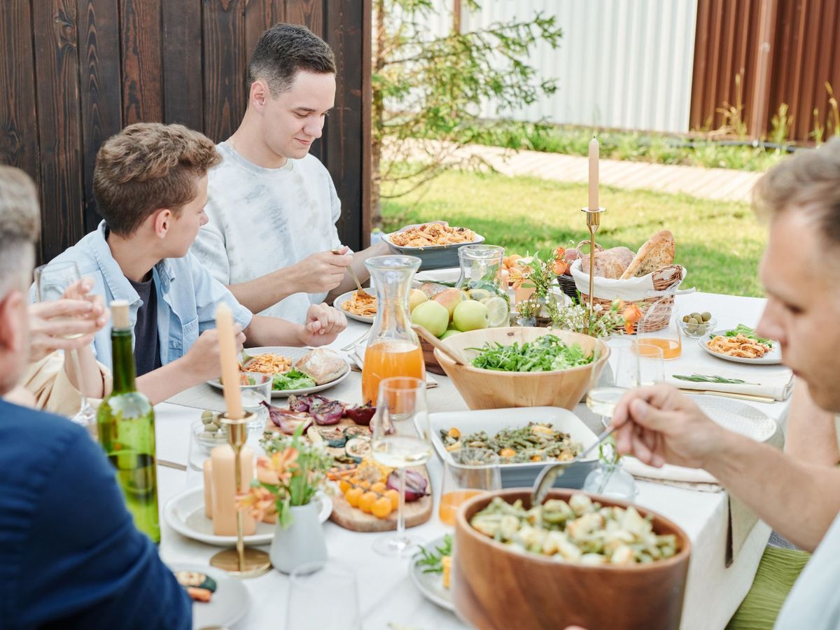 Group of lads sharing a long outdoor lunch with salads and fresh food