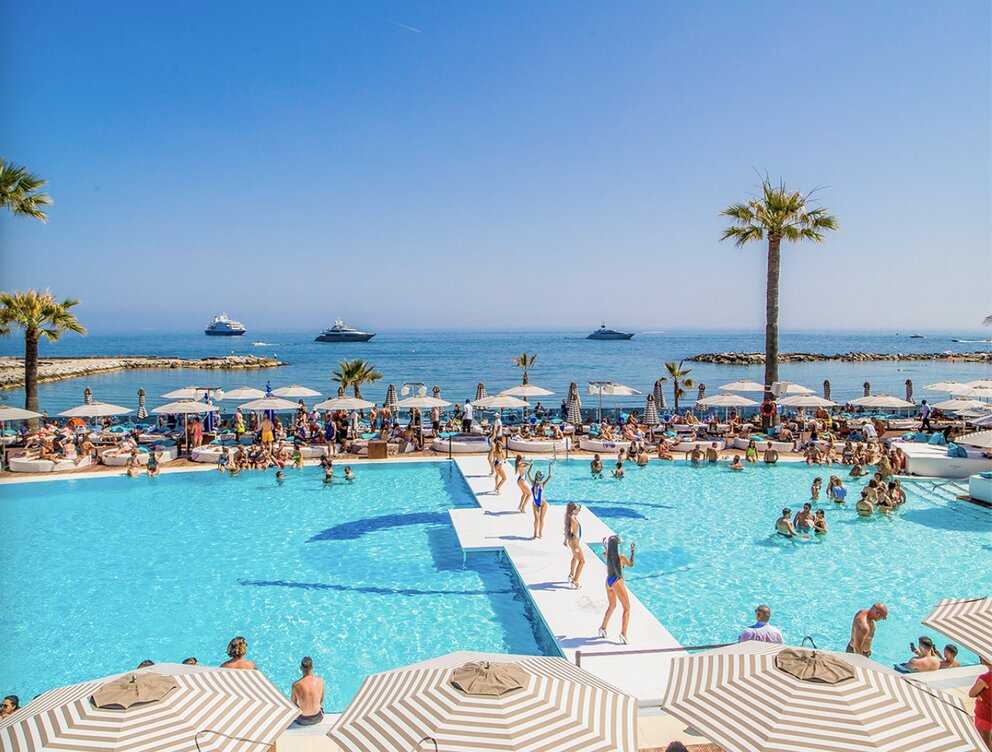 Sun loungers, umbrellas and a pool day party at a Marbella beach club with yachts anchored offshore