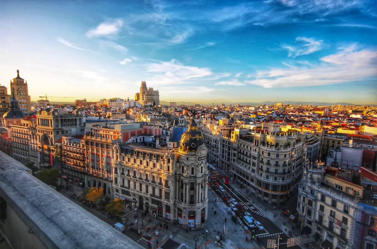 Aerial view of Madrid's Gran V&iacute;a at sunset, with the ornate domed Metropolis Building in the skyline.