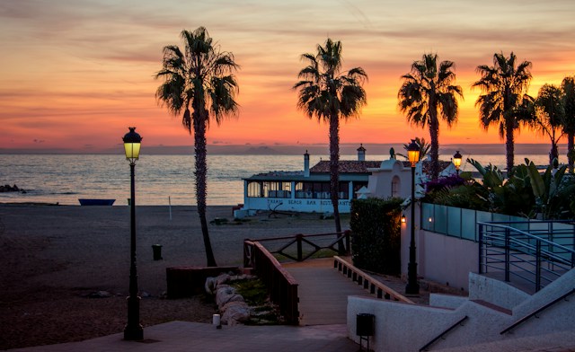 Sunset over the beach in Marbella with palm trees, street lamps and a beachfront restaurant