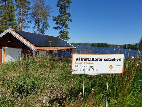 Bild på företagsskylt isatt i marken och hus med solpaneler i bakgrunden