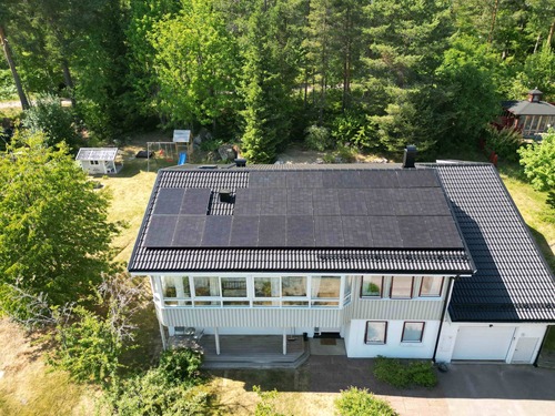 Vitt hus med solceller på taket sett från luften bland grönska