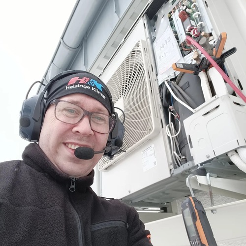 Servicetekniker från Helsinge Klimat med headset arbetar vid utomhusdel av luftvärmepump